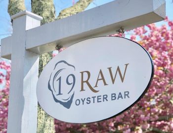 Sign of 19 Raw Oyster Bar in front of some pink trees
